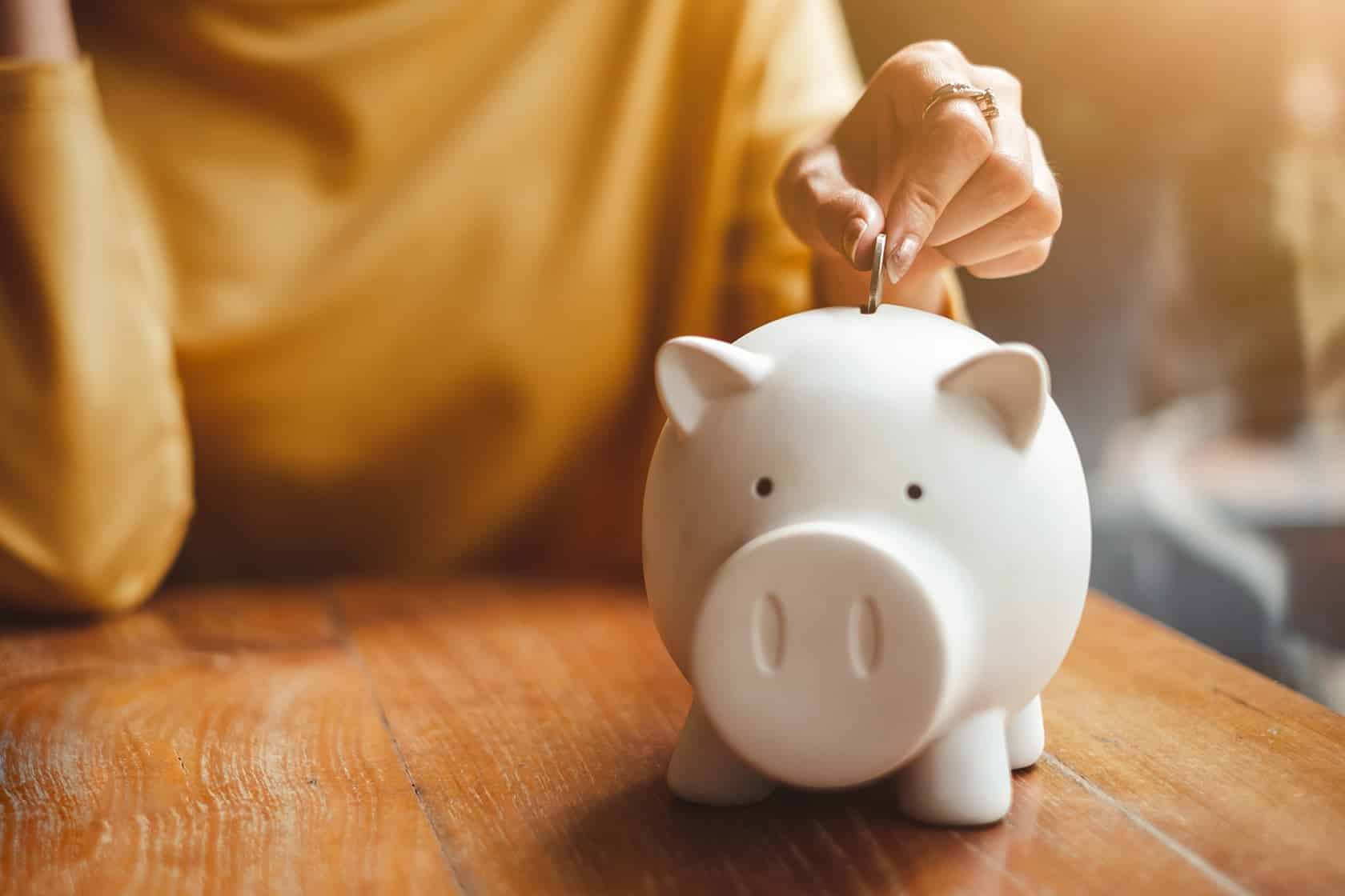 Hand einer junge Frau wirft Geld in Sparschwein